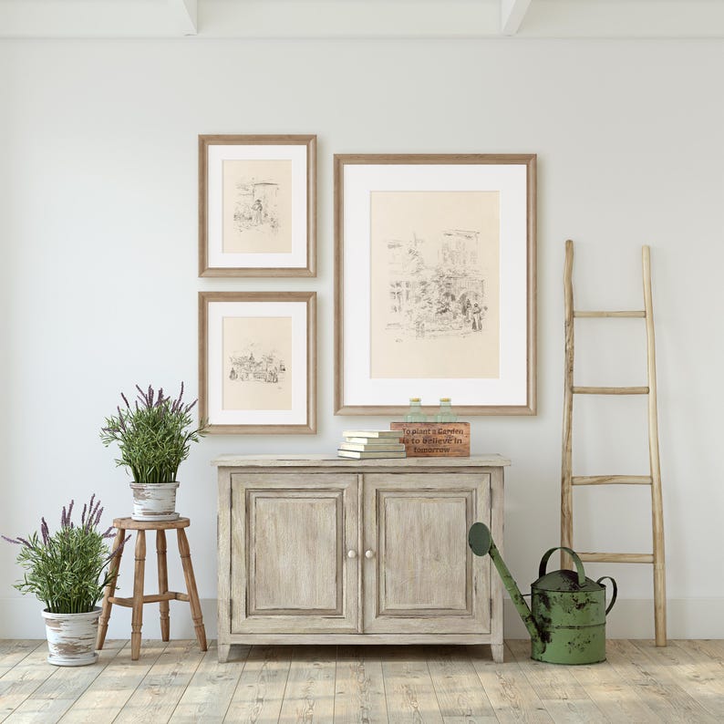 May include: A light wood cabinet with two doors, a wooden ladder, and three framed black and white drawings on a white wall. There are two potted plants with lavender flowers and a green watering can on the floor.