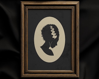 Pode incluir: Uma peça de arte de parede emoldurada com a silhueta preta de uma pessoa com cabelo encaracolado e uma madeixa branca proeminente, sobre um fundo oval de cor creme. A obra está inserida numa moldura de madeira castanha escura com acabamento texturado.