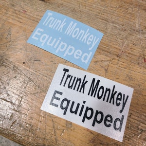 May include: Two stickers, one blue and one white, with the text "Trunk Monkey Equipped" in white and black lettering.