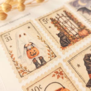 Op de afbeelding: Een vel met decoratieve stickers in postzegelstijl met Halloween-illustraties. E&eacute;n postzegel toont een kind in een spookkostuum met een pompoenemmer, een andere toont een zwarte kat bij een hek met herfstbladeren en een pompoen.