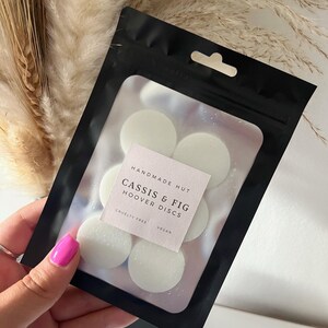 Peut inclure: Un sac refermable noir avec une fen&ecirc;tre transparente montrant six pastilles de cire rondes blanches. Le sac porte une &eacute;tiquette indiquant "Handmade Hut Cassis & Fig Hoover Discs Cruelty Free Vegan".