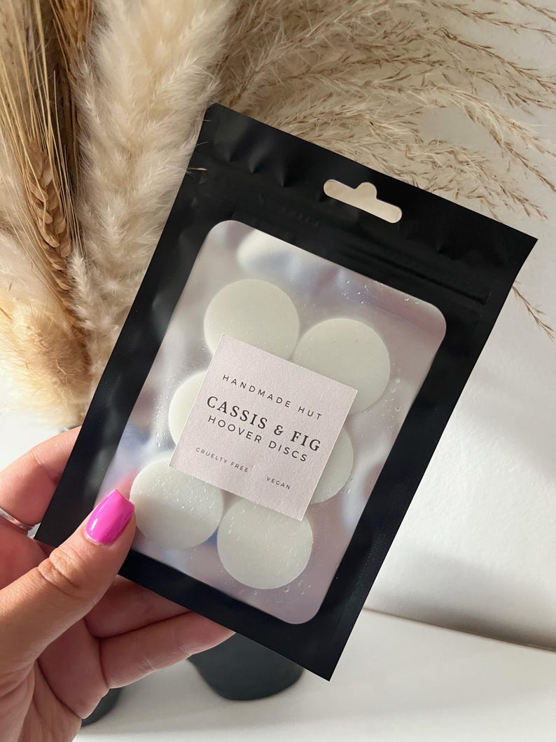 Peut inclure: Un sac refermable noir avec une fen&ecirc;tre transparente montrant six pastilles de cire rondes blanches. Le sac porte une &eacute;tiquette indiquant "Handmade Hut Cassis & Fig Hoover Discs Cruelty Free Vegan".