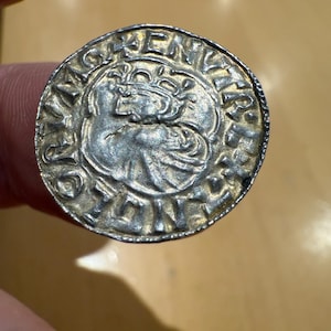 May include: A silver coin with a detailed design. The coin features a central image of a stylized animal or figure within a circular border, surrounded by text. The coin has a worn, antique appearance.