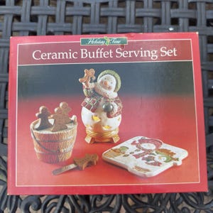 May include: A Holiday Time Ceramic Buffet Serving Set box featuring a snowman figurine, a wooden-style bucket with gingerbread-shaped picks, a gingerbread-shaped spreader, and a square plate with a snowman illustration on a red background.