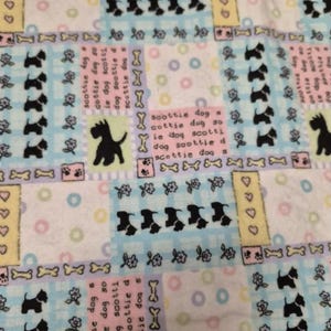 May include: A patterned fabric featuring a repeating design of black Scottie dog silhouettes, bones, flowers, and hearts. The fabric has a patchwork style with pastel blue, pink, and yellow squares. Text includes "scottie dog".