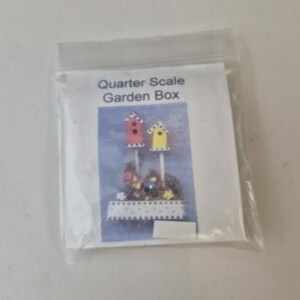 May include: A clear plastic bag containing a printed card with the text "Quarter Scale Garden Box." The card features a watercolor illustration of miniature birdhouses in red and yellow, with a garden scene below.