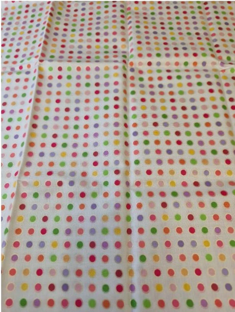 Op de afbeelding: Een witte stof met een herhalend patroon van kleine, gelijkmatig verdeelde stippen in diverse kleuren, waaronder roze, oranje, geel, groen en paars. Het textiel heeft een zichtbare geweven structuur en is in een rasterpatroon gerangschikt.