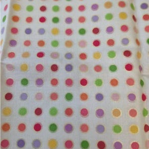 Op de afbeelding: Een witte stof met een herhalend patroon van kleine, gelijkmatig verdeelde stippen in diverse kleuren, waaronder rood, oranje, geel, lichtgroen en paars. De stippen zijn in een rastervorm over het gehele oppervlak gerangschikt.