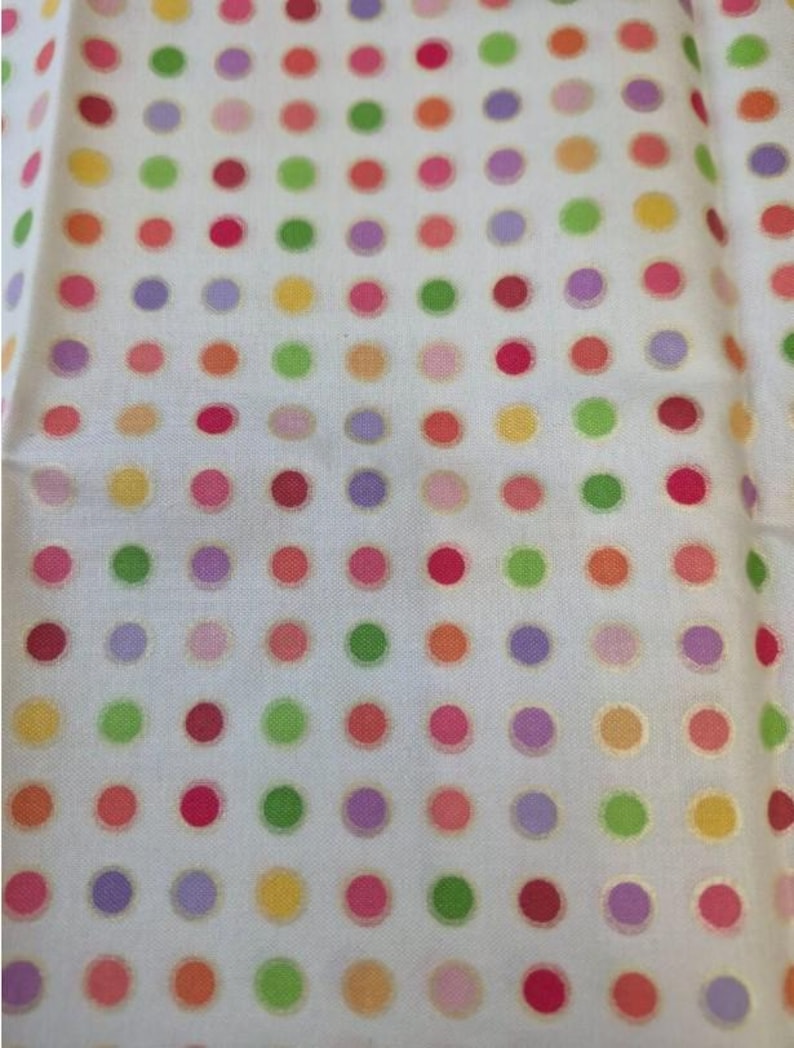 Op de afbeelding: Een witte stof met een herhalend patroon van kleine, gelijkmatig verdeelde stippen in diverse kleuren, waaronder rood, oranje, geel, lichtgroen en paars. De stippen zijn in een rastervorm over het gehele oppervlak gerangschikt.
