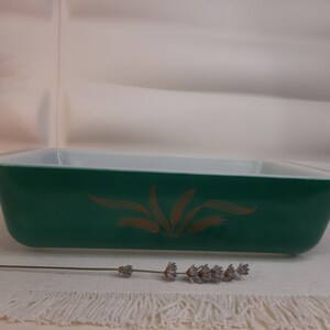 Puede incluir: Un plato para hornear de vidrio verde con un borde blanco y un diseño de trigo dorado.