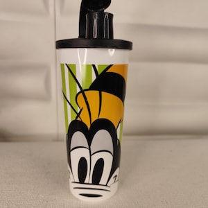 Puede incluir: Un vaso a rayas blancas y verdes con la cara de un personaje de dibujos animados. El vaso tiene una tapa negra con una abertura abatible. La cara del personaje es negra, blanca y amarilla.