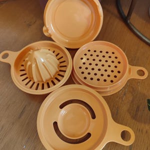 Puede incluir: Cuatro herramientas de cocina de plástico naranja con diferentes diseños. Las herramientas incluyen un exprimidor de cítricos, un rallador, un colador y una tapa.