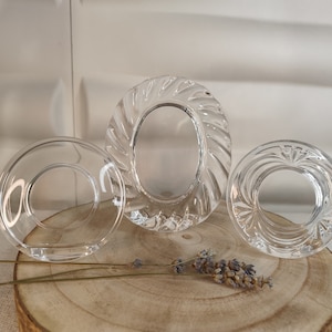 Puede incluir: Tres marcos de fotos de cristal transparente con bordes decorativos. Los marcos están dispuestos en fila sobre una superficie de madera.