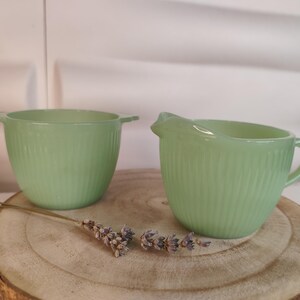 Puede incluir: Dos cuencos de vidrio verde claro y acanalado. Uno tiene dos asas, el otro un asa y un pico. Los cuencos están sobre una superficie de madera con lavanda seca.