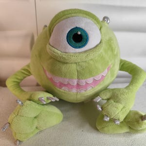 Può includere: Peluche verde con un grande occhio e un ghigno pieno di denti. Il giocattolo è un personaggio del film Monsters & Co.