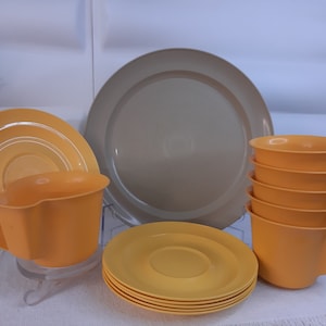 Könnte beinhalten: Ein Set aus gelben und beigefarbenen Plastikgeschirr, bestehend aus einer großen Platte, vier kleineren Tellern und vier Tassen. Die Tassen haben eine einzigartige geschwungene Form.