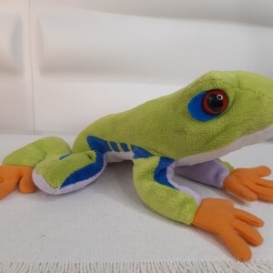 May include: Green plush frog toy with blue and yellow stripes, orange feet, and red eyes.