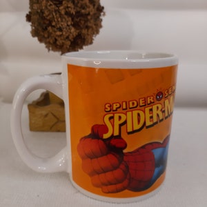Op de afbeelding: Witte keramische mok met een feloranje achtergrond waarop een rode en blauwe Spiderman-illustratie is afgebeeld. De tekst "Spider-Sense" en "Spider-Man" is in zwart gedrukt.