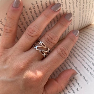 May include: A silver ring featuring a geometric design. The ring is crafted from interlocking squares and rectangles, creating a contemporary and abstract style.