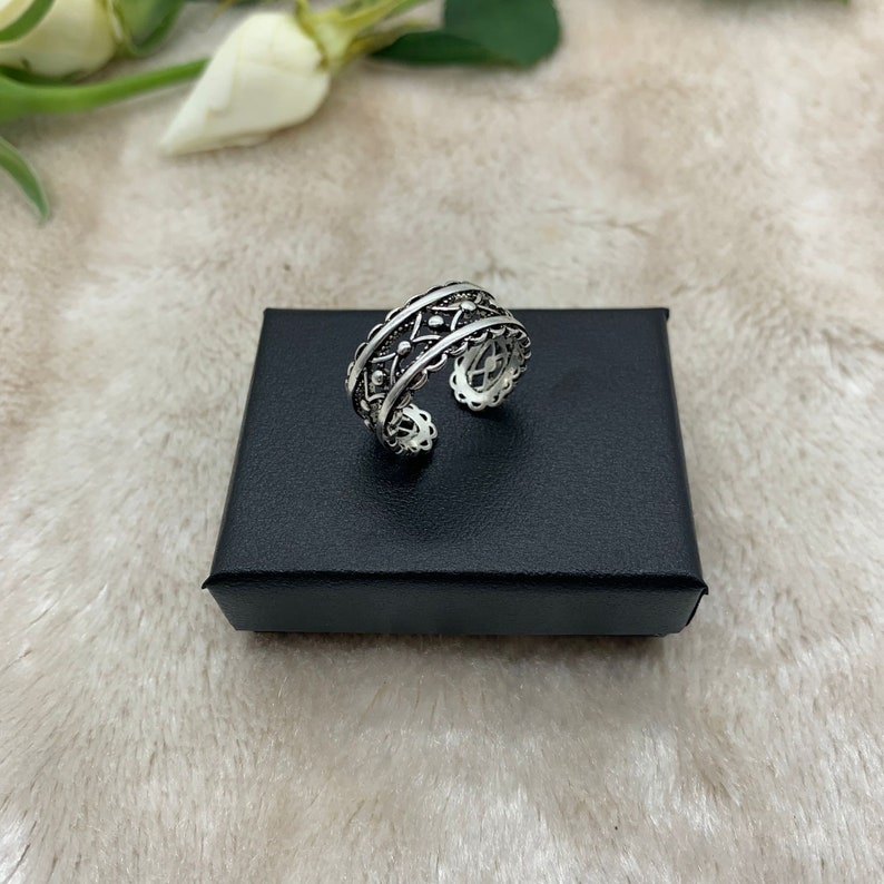 Pu&ograve; includere: Un anello d'argento con un design intricato che presenta un motivo ripetitivo di piccoli cerchi e linee. L'anello &egrave; su una scatola di velluto nero.