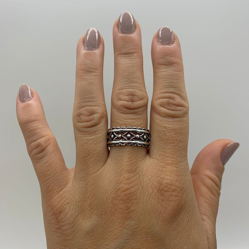 Pu&ograve; includere: Un anello d'argento con un design dettagliato che presenta piccoli cerchi e una fascia testurizzata.
