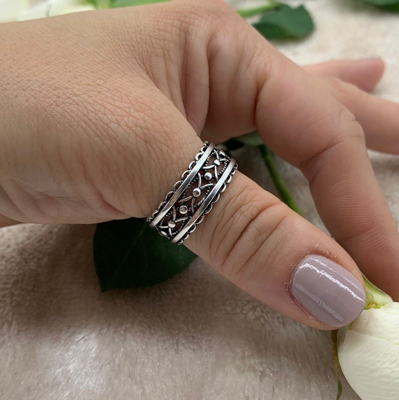 Pu&ograve; includere: Un anello d'argento con un design delicato e intricato. L'anello &egrave; largo e presenta un motivo ripetitivo di piccoli cerchi e triangoli.
