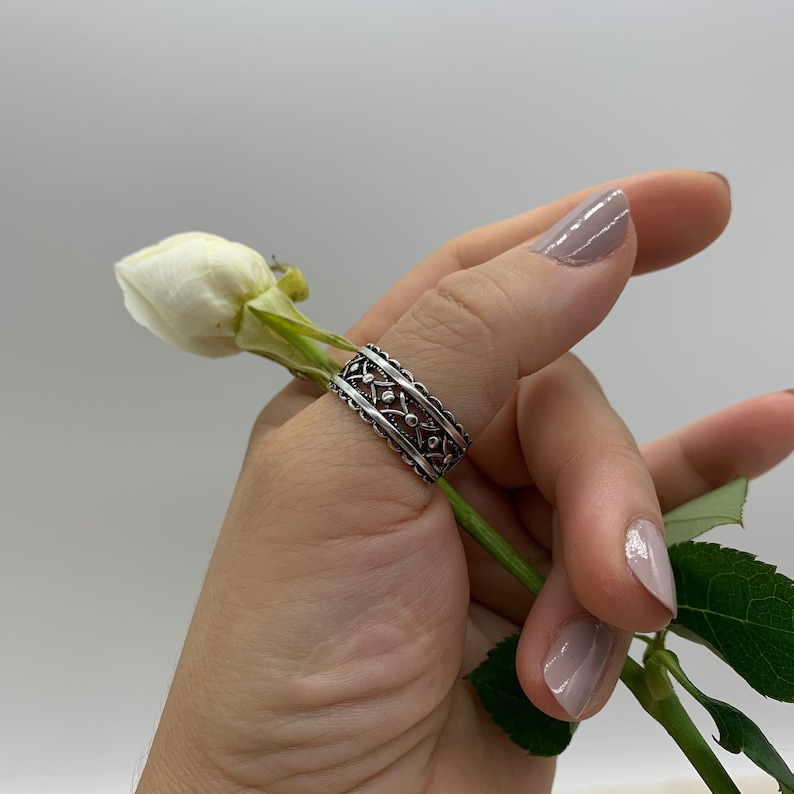 Pu&ograve; includere: Un anello per il pollice in argento con un design delicato e intricato. L'anello &egrave; indossato sul pollice di una persona, e il design presenta un motivo ripetitivo di piccoli cerchi e linee curve.