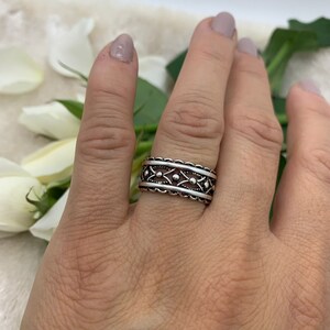 Pu&ograve; includere: Un anello d'argento con un design dettagliato e intricato. L'anello ha una fascia larga con un motivo ripetitivo di piccoli cerchi e diamanti.