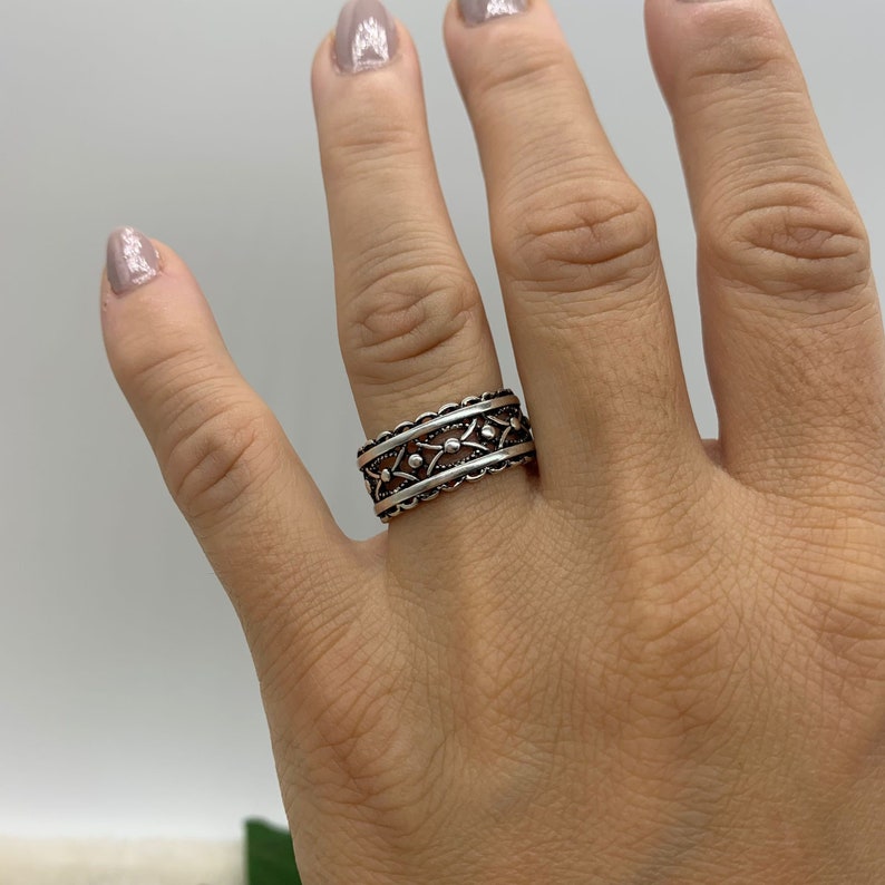 Pu&ograve; includere: Un anello d'argento con un designo dettagliato che presenta un motivo ripetitivo di piccoli cerchi e linee curve.