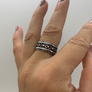 Pu&ograve; includere: Un anello d'argento con un design delicato e intricato che presenta piccoli cerchi e un motivo ripetitivo. L'anello &egrave; indossato su un dito.
