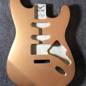 Könnte beinhalten: Ein kupferfarbener E-Gitarrenkorpus mit einem weißen Etikett, auf dem "White Star" und "134363" steht.