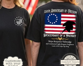 Op de afbeelding: Zwarte T-shirts met patriottische ontwerpen. Eén shirt heeft een wit embleem met "1776" en sterren. De andere toont een vlagontwerp met de tekst: "250th Anniversary of Freedom" en "Descendant of a Patriot."