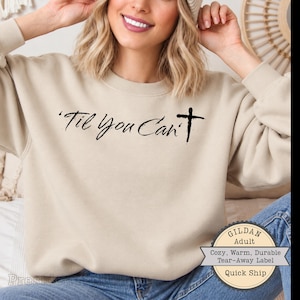 May include: A beige crewneck sweatshirt featuring the black text 'Til You Can't' with a cross symbol replacing the letter 't'. The garment has long sleeves and a ribbed neckline, presented in a neutral tone with a clear, bold graphic print.