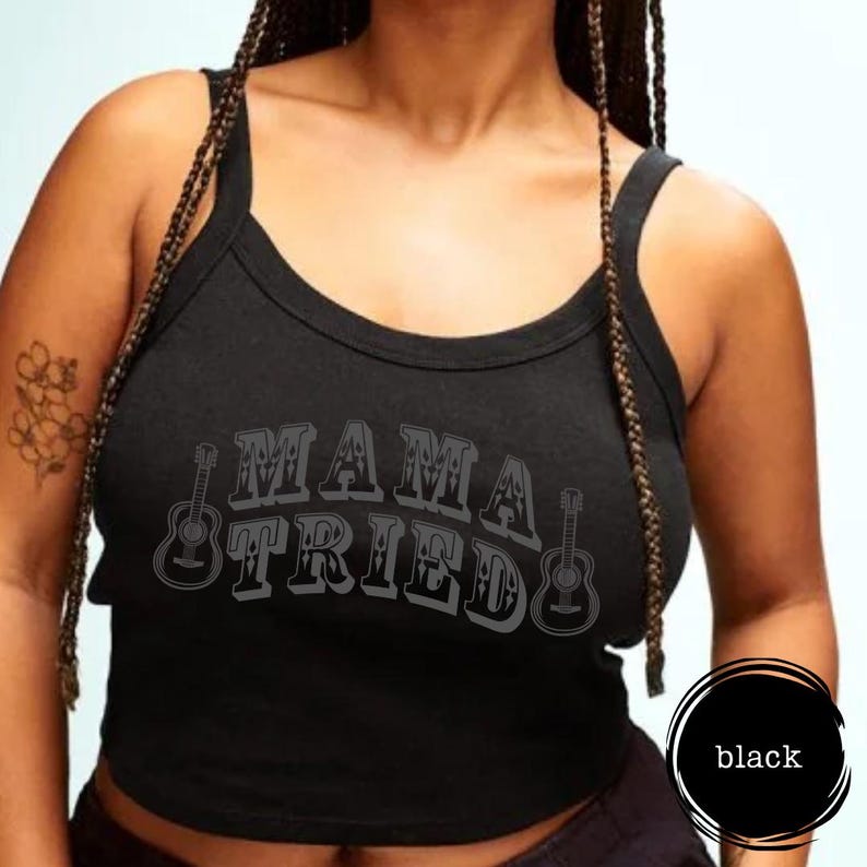 May include: Black tank top with the text "MAMA TRIED" in a distressed font, accompanied by guitar illustrations. The top has a scoop neckline and wide straps. The word "black" is in a circle on the bottom right.