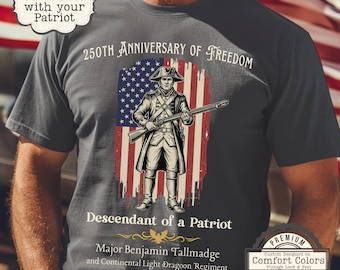 May include: Dark gray t-shirt featuring a patriotic design. The shirt displays an illustration of a soldier in front of an American flag, with text that reads "250th Anniversary of Freedom" and "Descendant of a Patriot."