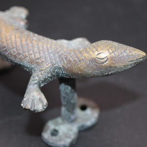 Op de afbeelding: Een bronzen hagedis deurknop met een getextureerd oppervlak en een gedetailleerd oog. De knop is gemonteerd op een basis met een decoratief ontwerp.