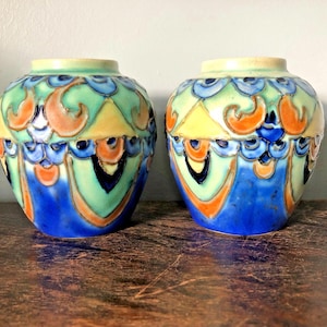 May include: Two ceramic vases with a rounded shape and a short neck. The surface features a raised, embossed pattern in shades of blue, light green, yellow, and orange, with a glossy finish that highlights the intricate, repeating decorative motifs.