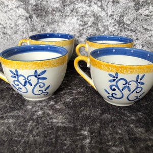 Op de afbeelding: Set van vier witte keramische mokken met blauwe en gele bloemenmotieven. De mokken hebben een afgeronde vorm en een handvat.