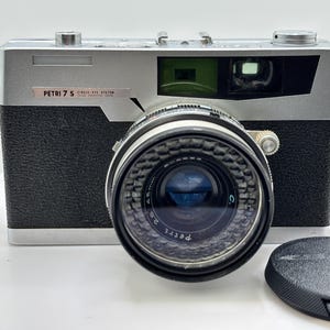 May include: A vintage Petri 7 S single-lens reflex camera with a black leatherette body and silver top. The lens is black with silver rings and the lens cap is black. The camera has a 45mm lens.