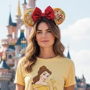 May include: A yellow t-shirt featuring a graphic of Belle and a red sequined bow headband with gold ears decorated with floral patterns and character illustrations. The headband has a large, central red sequin bow and circular ears.