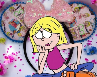 May include: A black headband with attached mouse ears and a bow. The ears are light pink with a cartoon print and blue trim. The bow is covered in pink sequins. A cartoon character is in the foreground.