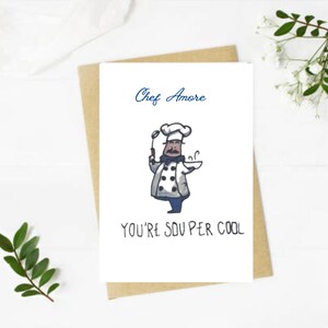 May include: A white greeting card with a cartoon chef illustration. The text "Chef Amore" is above the chef, and "YOU'RE SOUPer COOL" is below. The card is on a brown envelope.