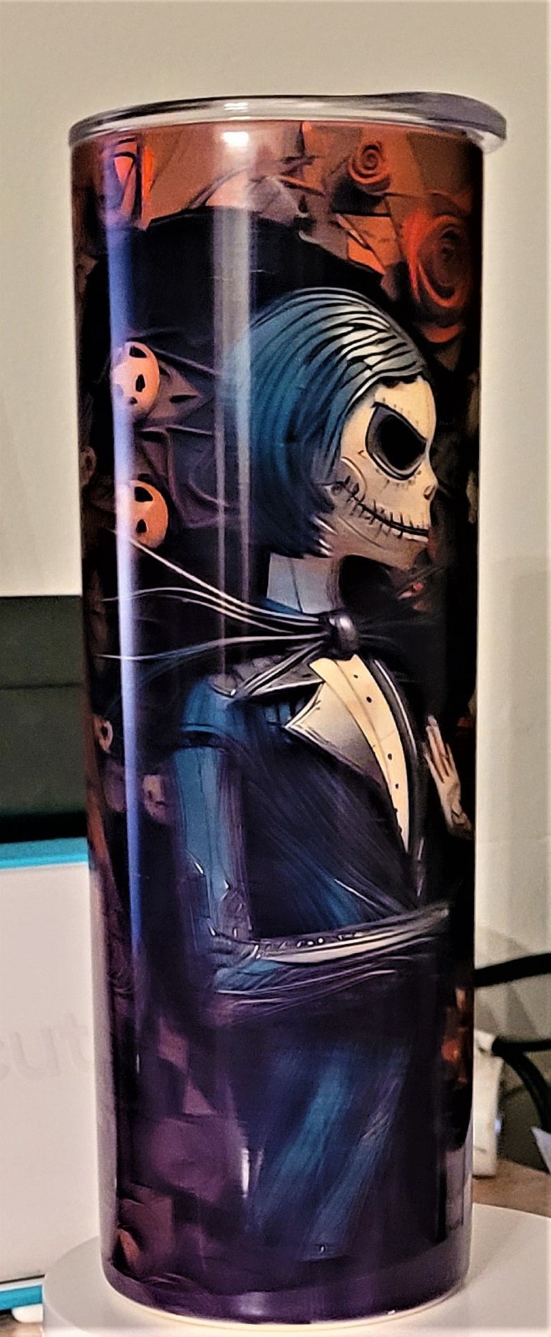 Pu&ograve; includere: Un bicchiere in acciaio inossidabile con un'immagine in bianco e nero di Jack Skellington del film Nightmare Before Christmas. L'immagine mostra Jack in completo con papillon e camicia bianca. Lo sfondo &egrave; di colore viola scuro e arancione con un motivo floreale.