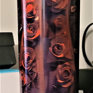 Pu&ograve; includere: Un bicchiere alto in acciaio inossidabile con un motivo di rose nere e arancioni. Il bicchiere ha un coperchio trasparente e una base argentata.