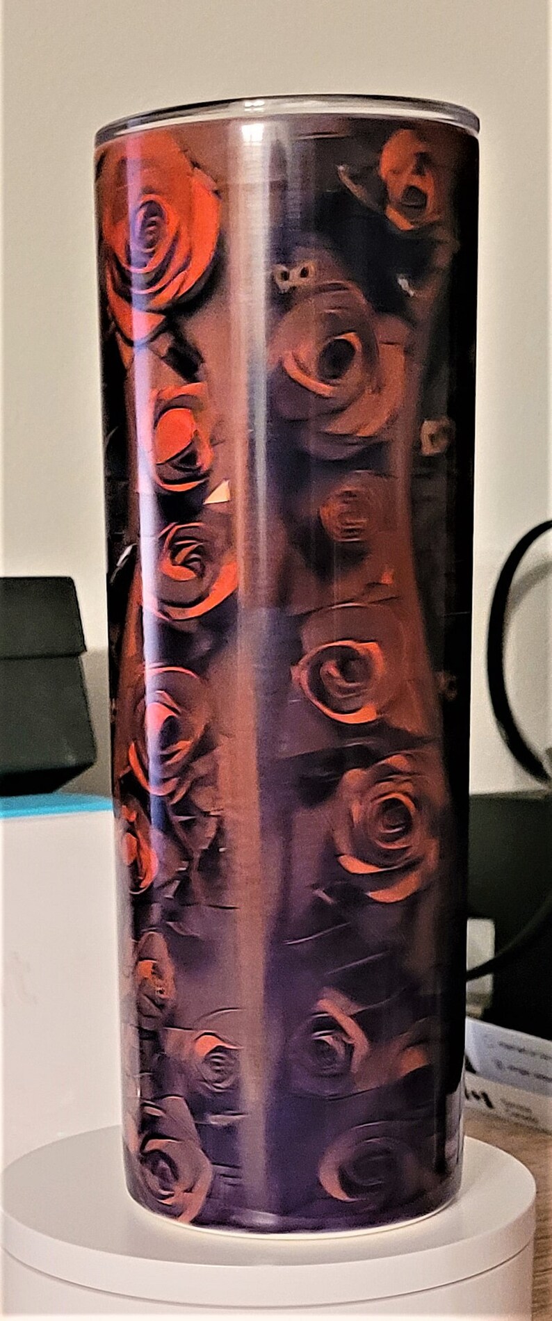 Pu&ograve; includere: Un bicchiere alto in acciaio inossidabile con un motivo di rose nere e arancioni. Il bicchiere ha un coperchio trasparente e una base argentata.