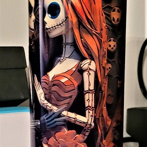 Pu&ograve; includere: Un bicchiere in acciaio inossidabile con un design nero e arancione che presenta una coppia di scheletri. La donna indossa un vestito rosso e ha lunghi capelli rossi. L'uomo indossa un abito nero e un cappello a cilindro nero. Il design &egrave; ispirato al film "Nightmare Before Christmas".