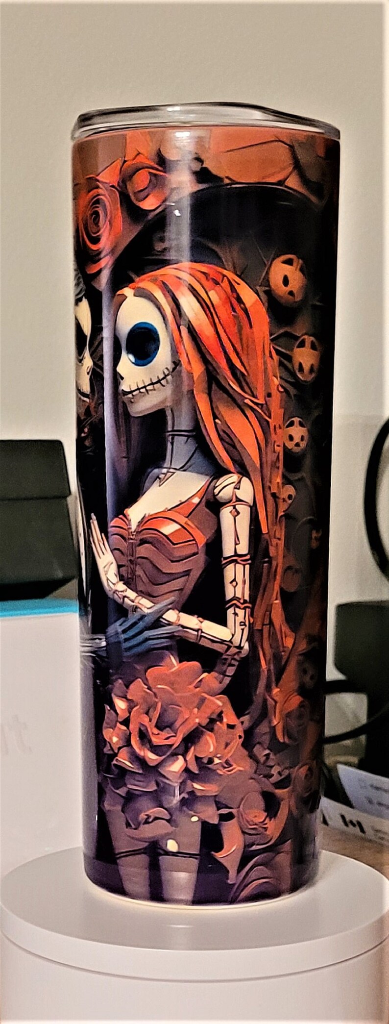 Pu&ograve; includere: Un bicchiere in acciaio inossidabile con un design nero e arancione che presenta una coppia di scheletri. La donna indossa un vestito rosso e ha lunghi capelli rossi. L'uomo indossa un abito nero e un cappello a cilindro nero. Il design &egrave; ispirato al film "Nightmare Before Christmas".