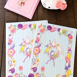 May include: Two translucent plastic document folders featuring a light blue and white vertical striped pattern decorated with illustrations of colorful parakeets, cockatiels, and various pink and purple flowers arranged in wreaths and borders.