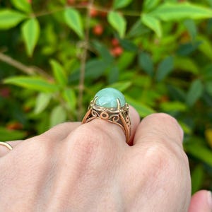 May include: A gold ring with a large, round, light green gemstone set in a delicate, ornate design.