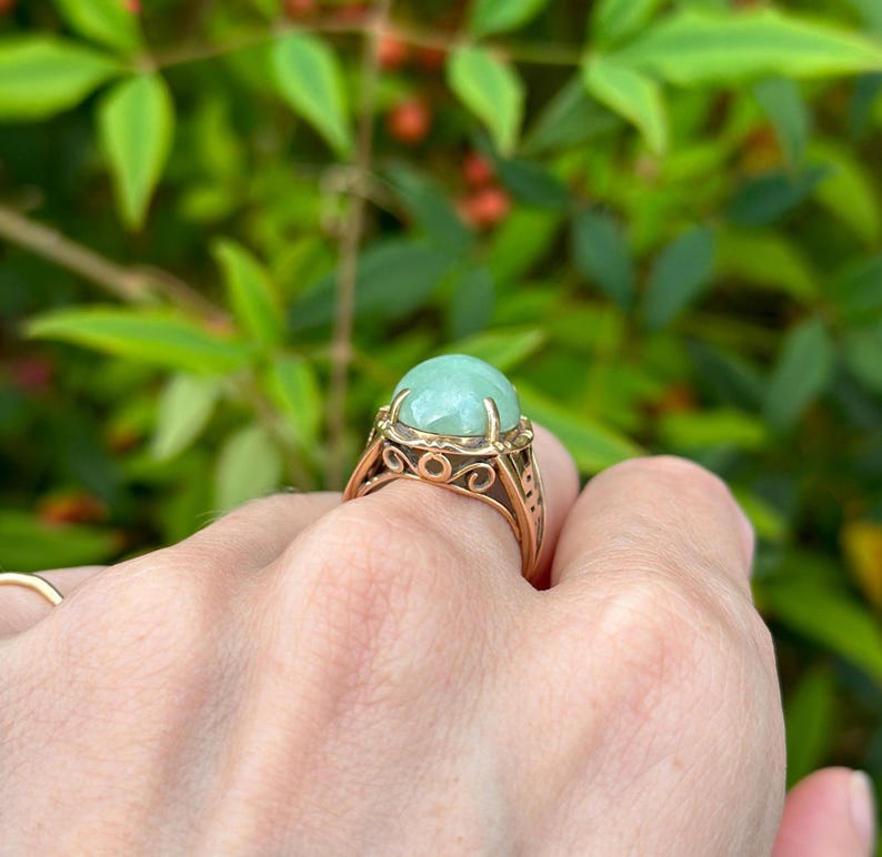 May include: A gold ring with a large, round, light green gemstone set in a delicate, ornate design.